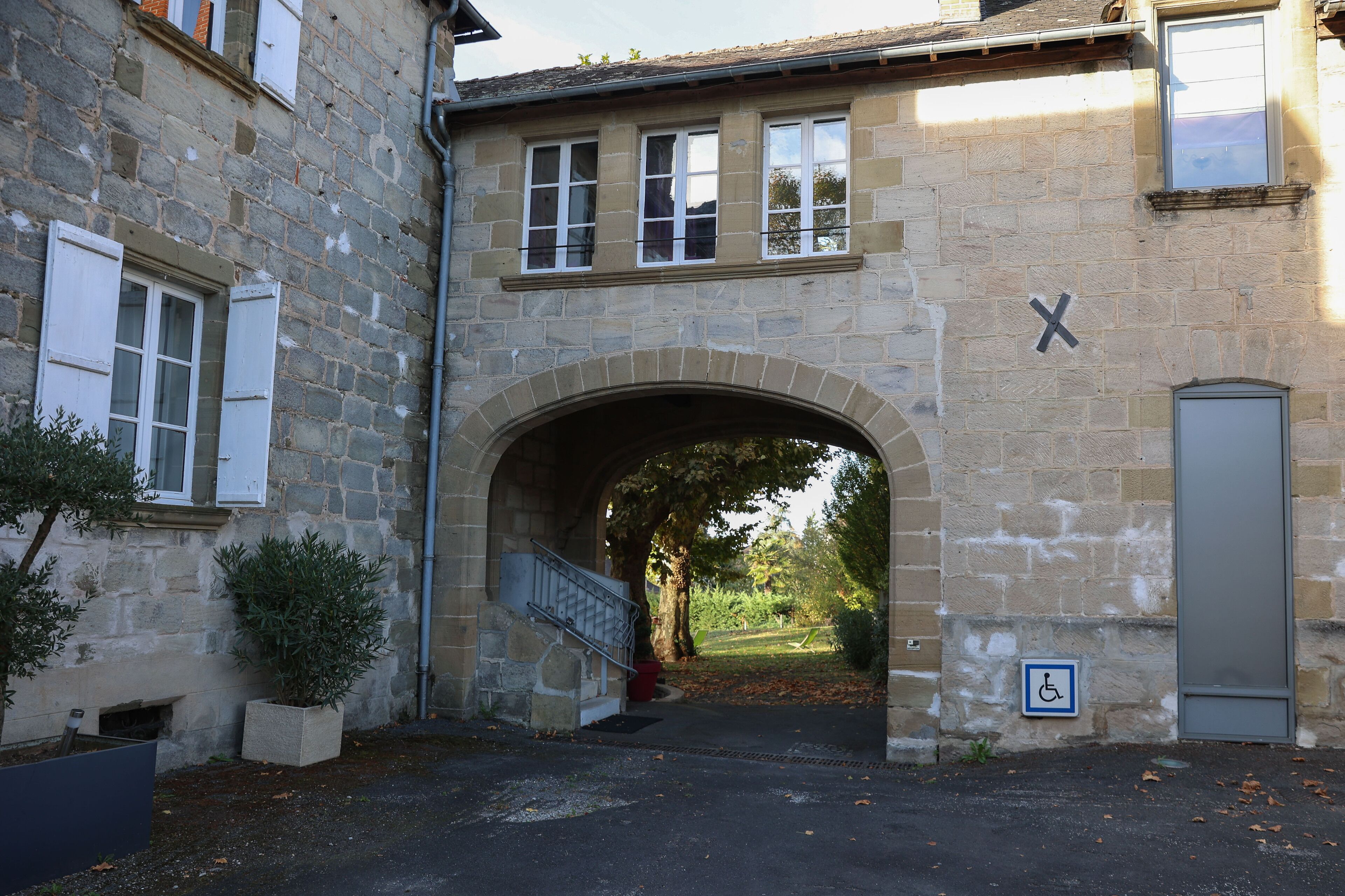 Un edificio in pietra con un ingresso ad arco, il segnale di accessibilità per carrozzina e una piccola scala che conduce a una porta.