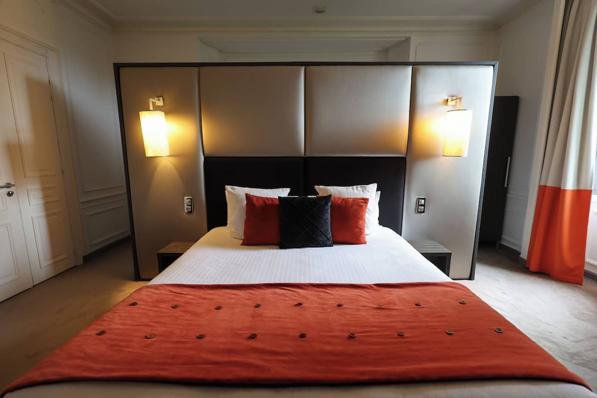 A hotel room with a large bed, two bedside tables, a wardrobe, and two wall-mounted lights.