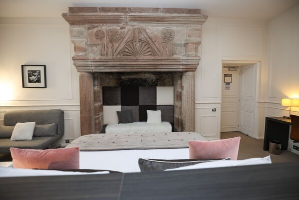 A hotel room with a large bed, a fireplace, a sofa, and a framed picture on the wall. - Hôtel Château Lacan (Brive-la-Gaillarde)