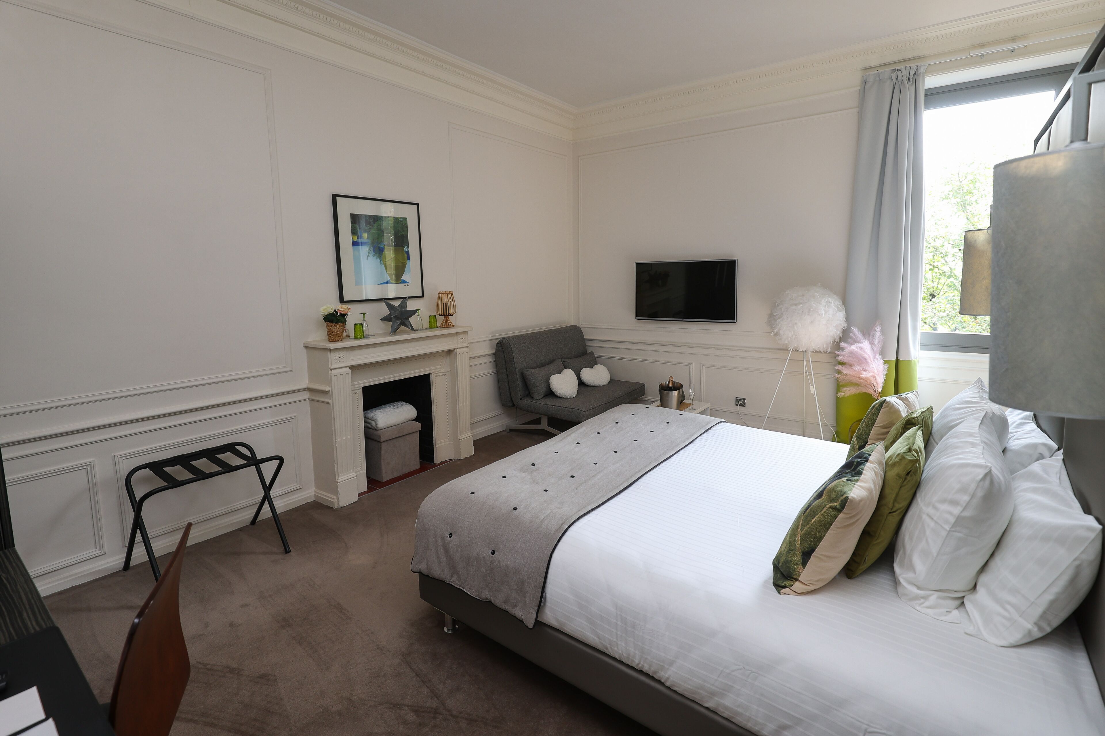 A bedroom with a bed, a TV, a fireplace, and a window with curtains.