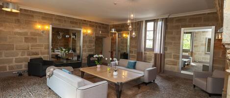 A spacious living room with a stone wall, a large mirror, and a modern chandelier.