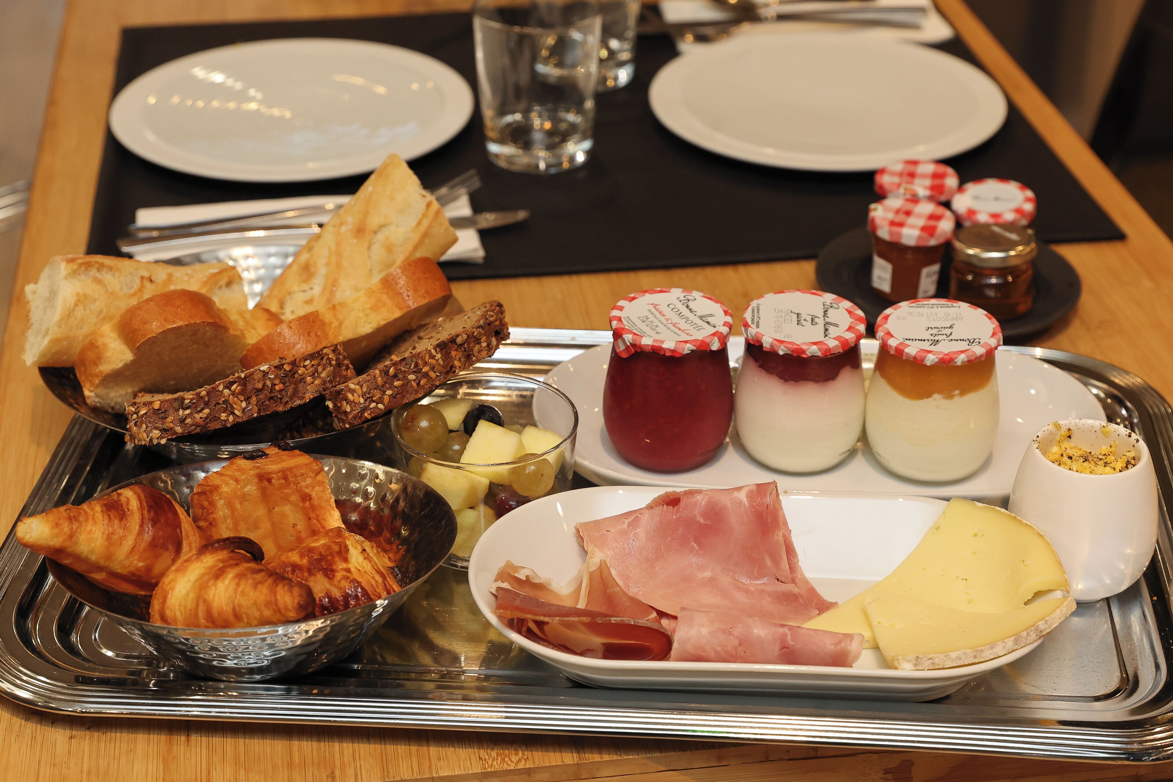A breakfast tray with croissants, cheese, ham, and jams.