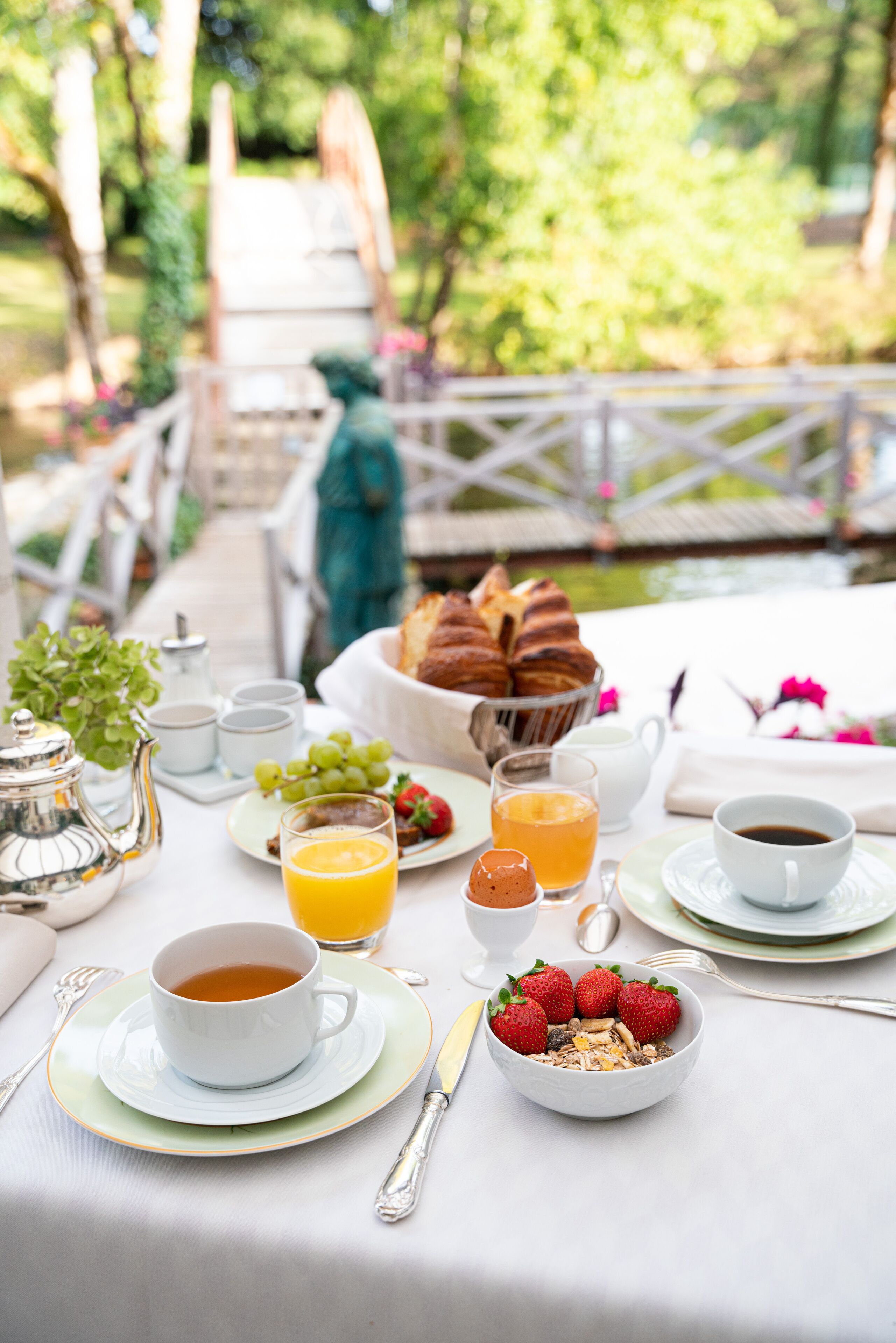 A breakfast table set outdoors with a variety of food items, including bread, fruit, and beverages.