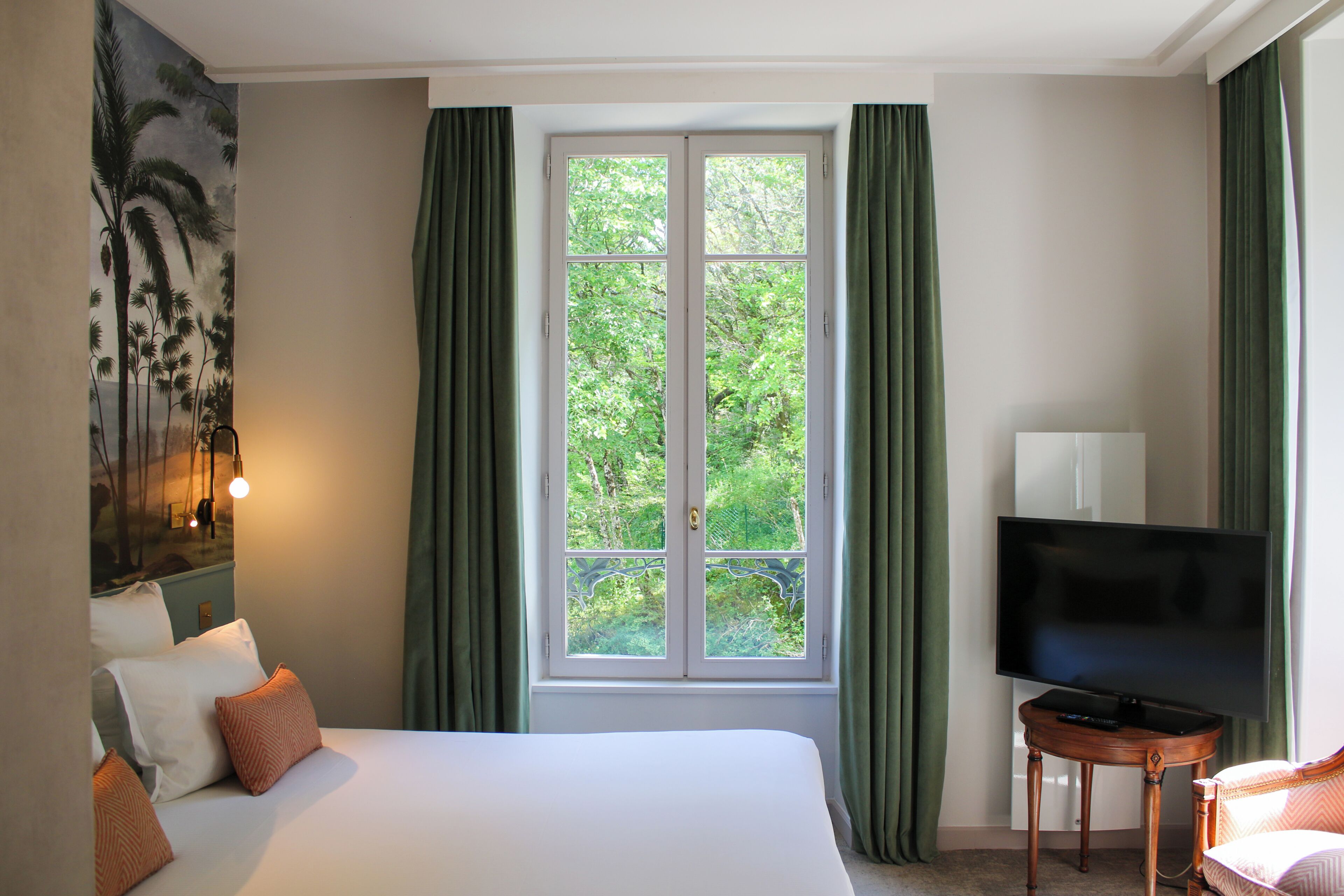 Une chambre d’hôtel avec un lit, une télévision, une fenêtre avec des rideaux et un tableau au mur.