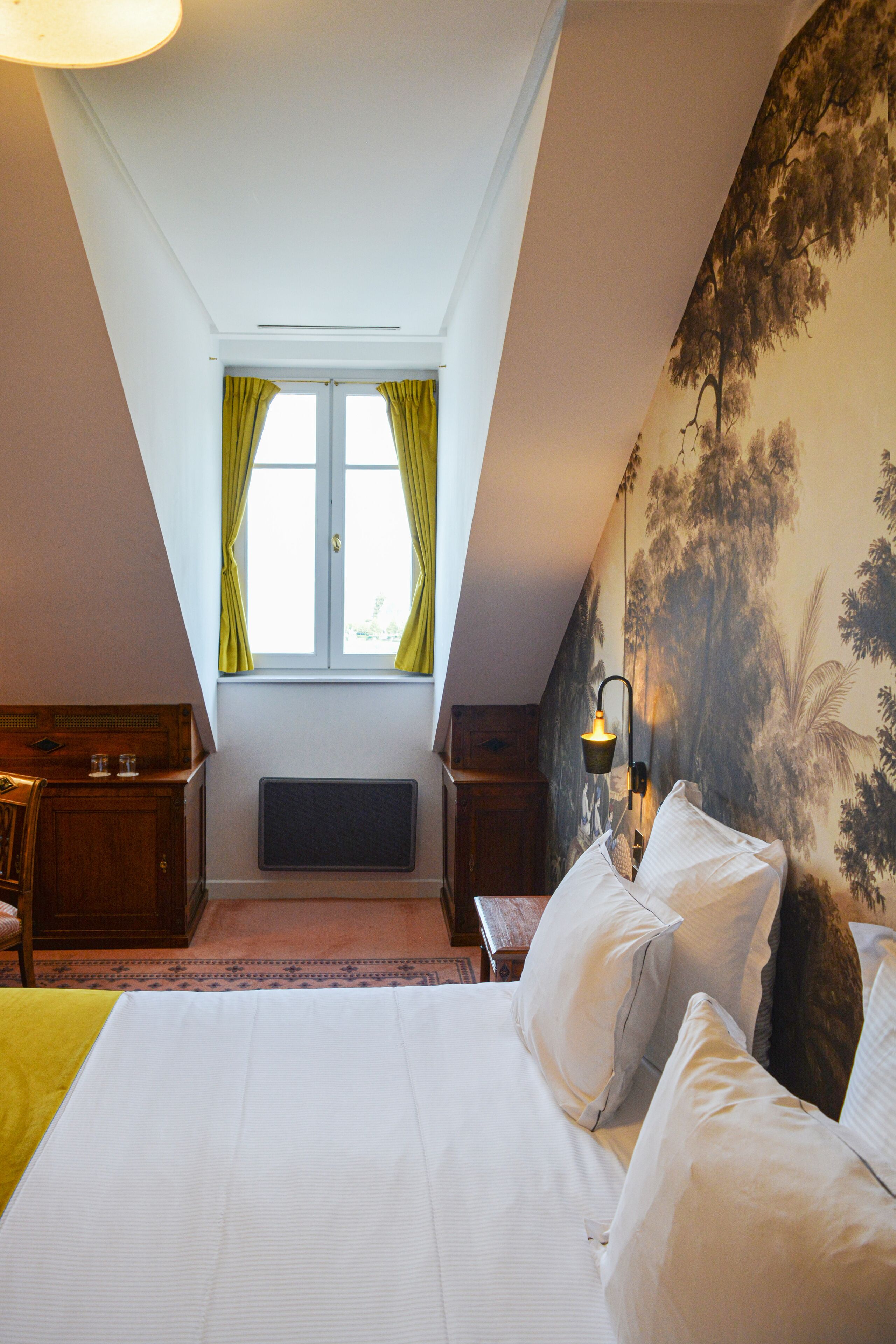 Ein Schlafzimmer mit einem großen Bett, einem Fenster mit Vorhängen, einem Heizkörper und einer Wand mit einer Baummalerei.
