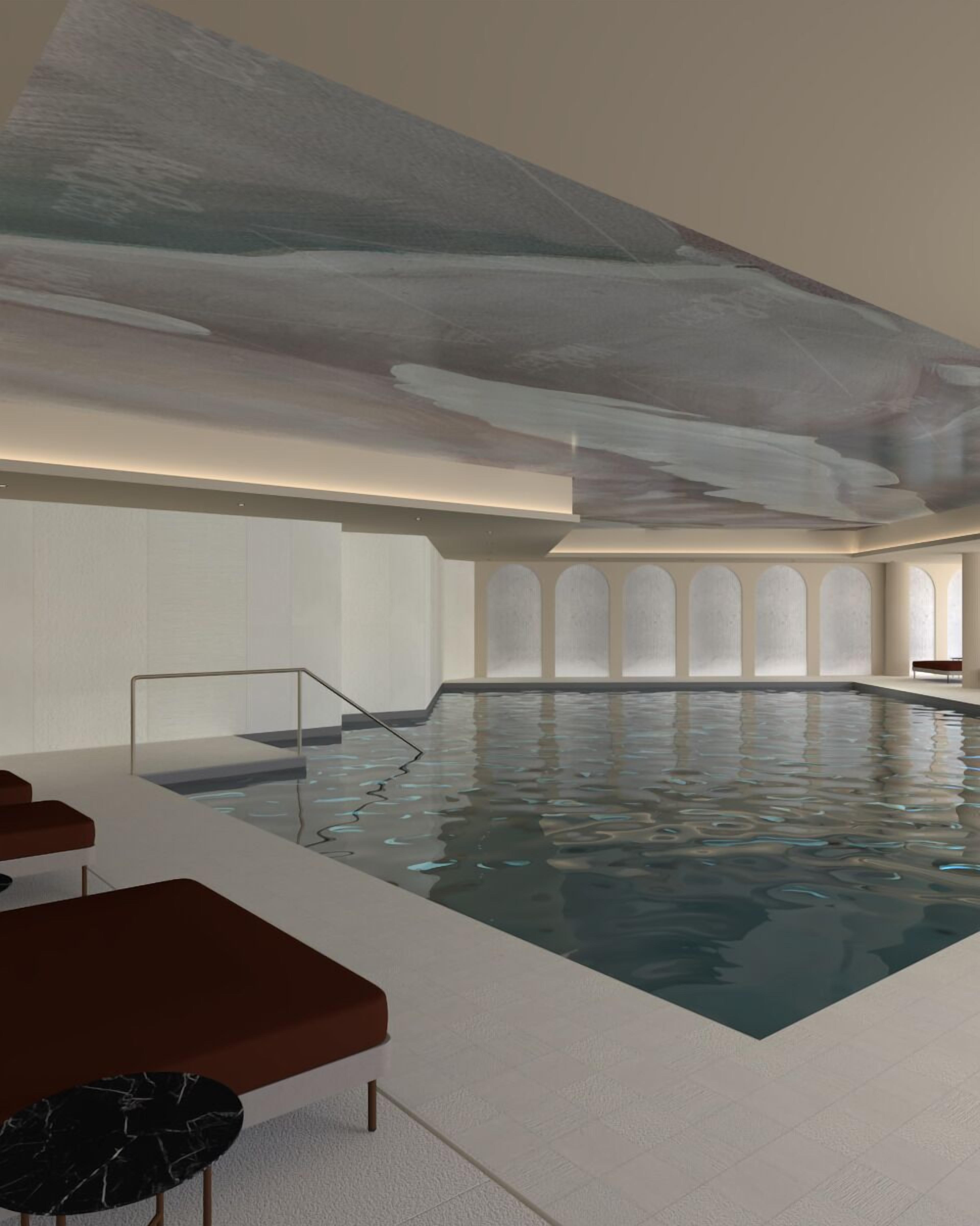 A modern indoor swimming pool with a minimalist design, featuring a clear glass barrier and a few red cushioned seating areas.