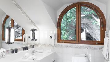 Une salle de bain moderne avec un grand miroir, une baignoire et une fenêtre donnant sur un paysage verdoyant.