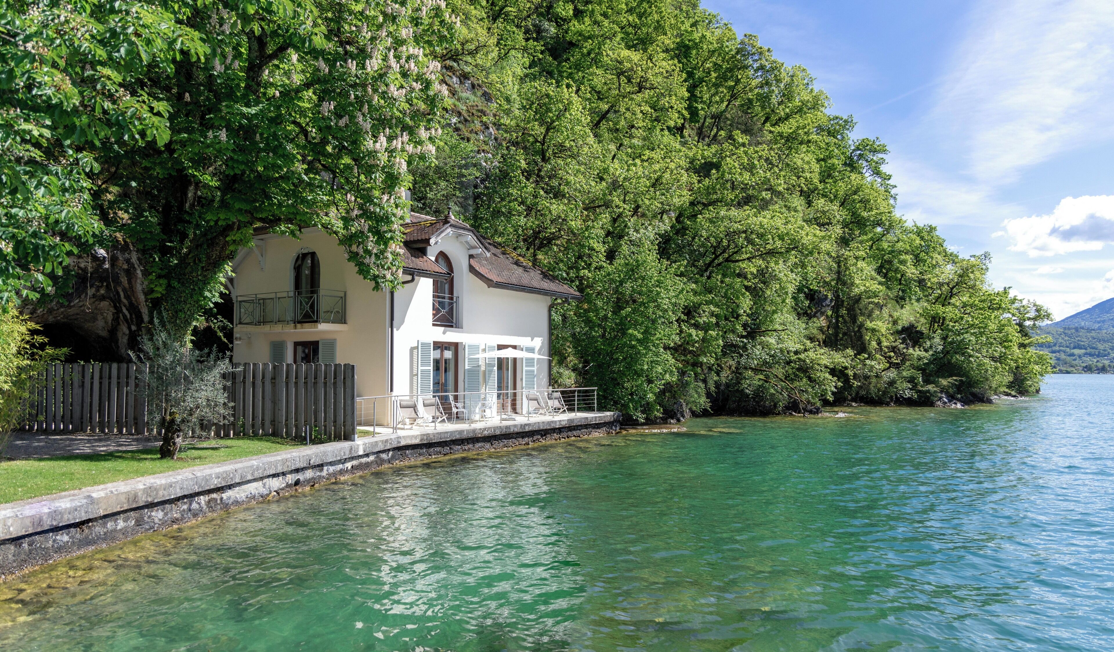 A lakeside house with a balcony, a wooden fence, and a clear view of the lake.