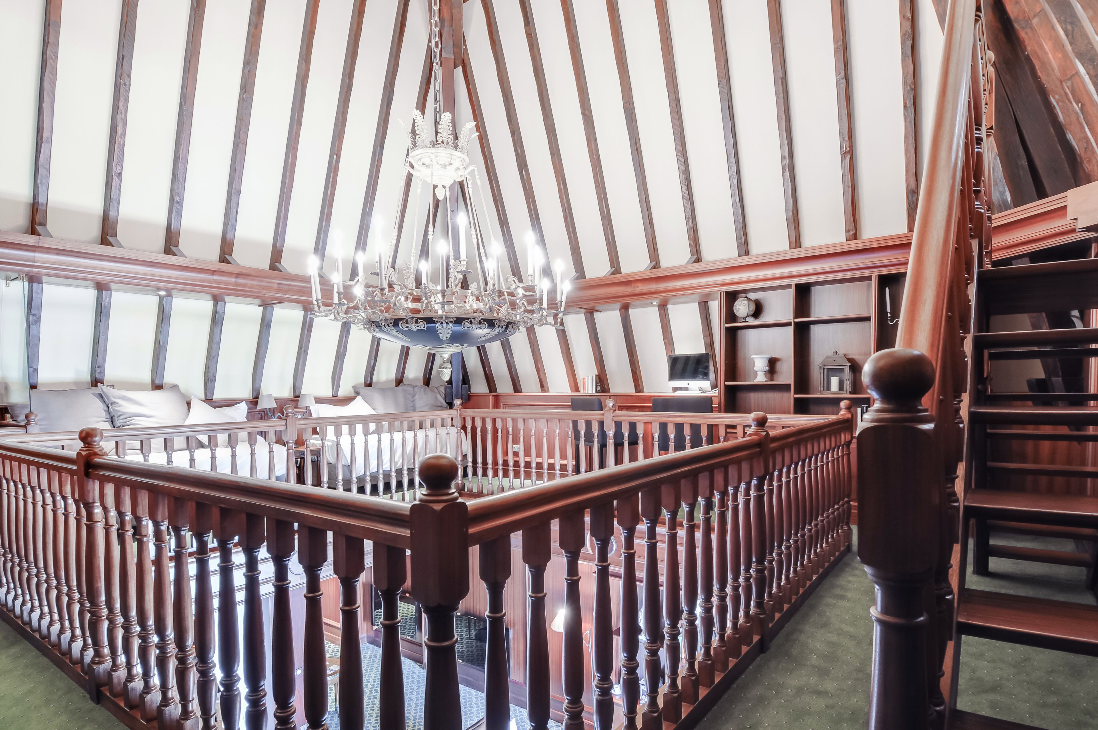 A grand room with a high ceiling, a chandelier, wooden railings, and a staircase.