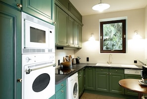 A kitchen with green cabinets, a washing machine, a microwave, and a sink.