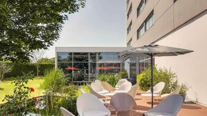 An outdoor seating area with modern chairs and a table, surrounded by greenery and a building with large windows.