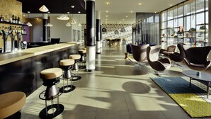A modern bar area with stools, a counter, and a seating area with chairs.
