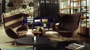 A modern living room with two brown chairs, a round coffee table, a sofa, and a bookshelf.