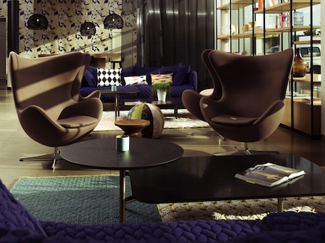 A modern living room with two brown chairs, a round coffee table, a sofa, and a bookshelf.