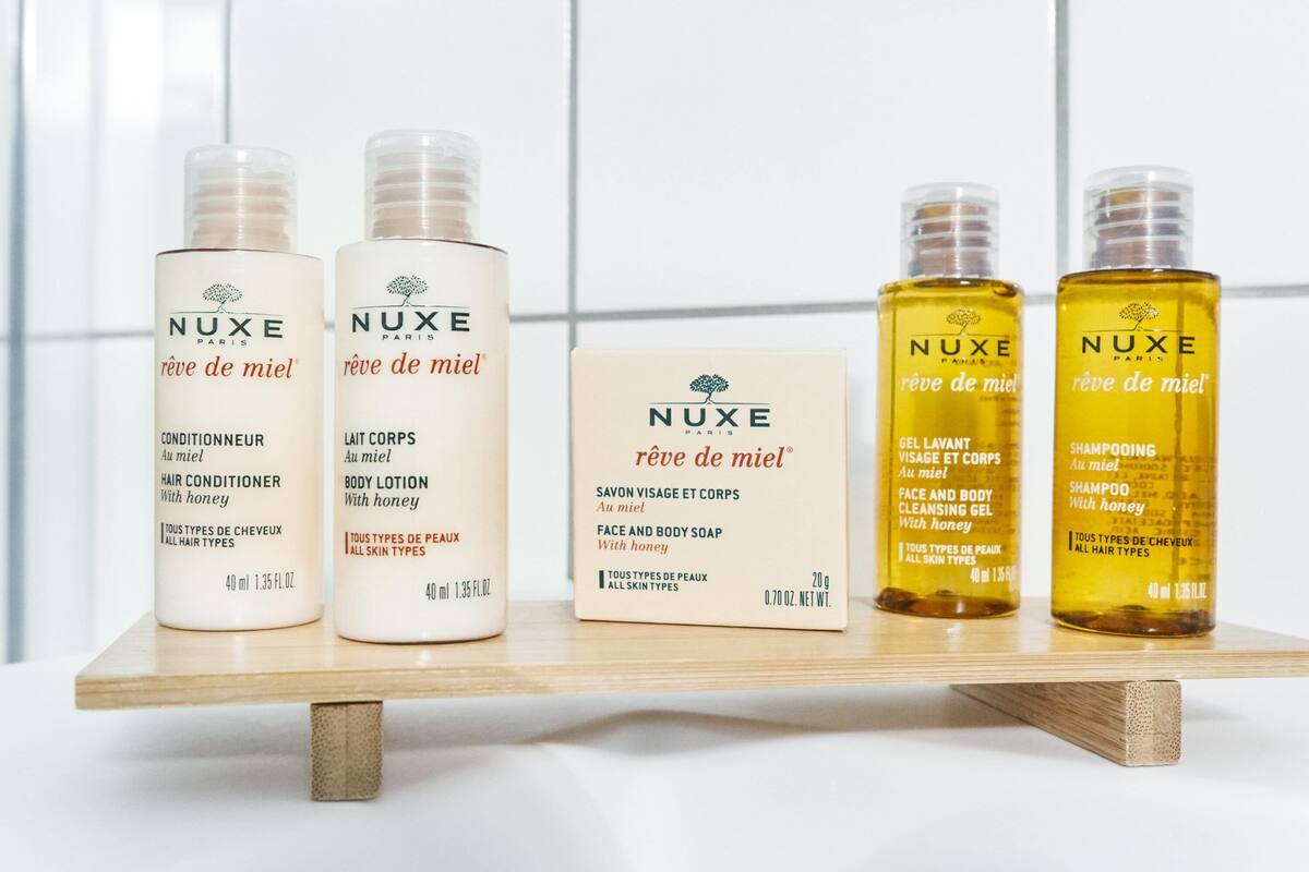 A display of NUXE Paris hair conditioner, body lotion, face and body soap, and shampoo on a wooden shelf.