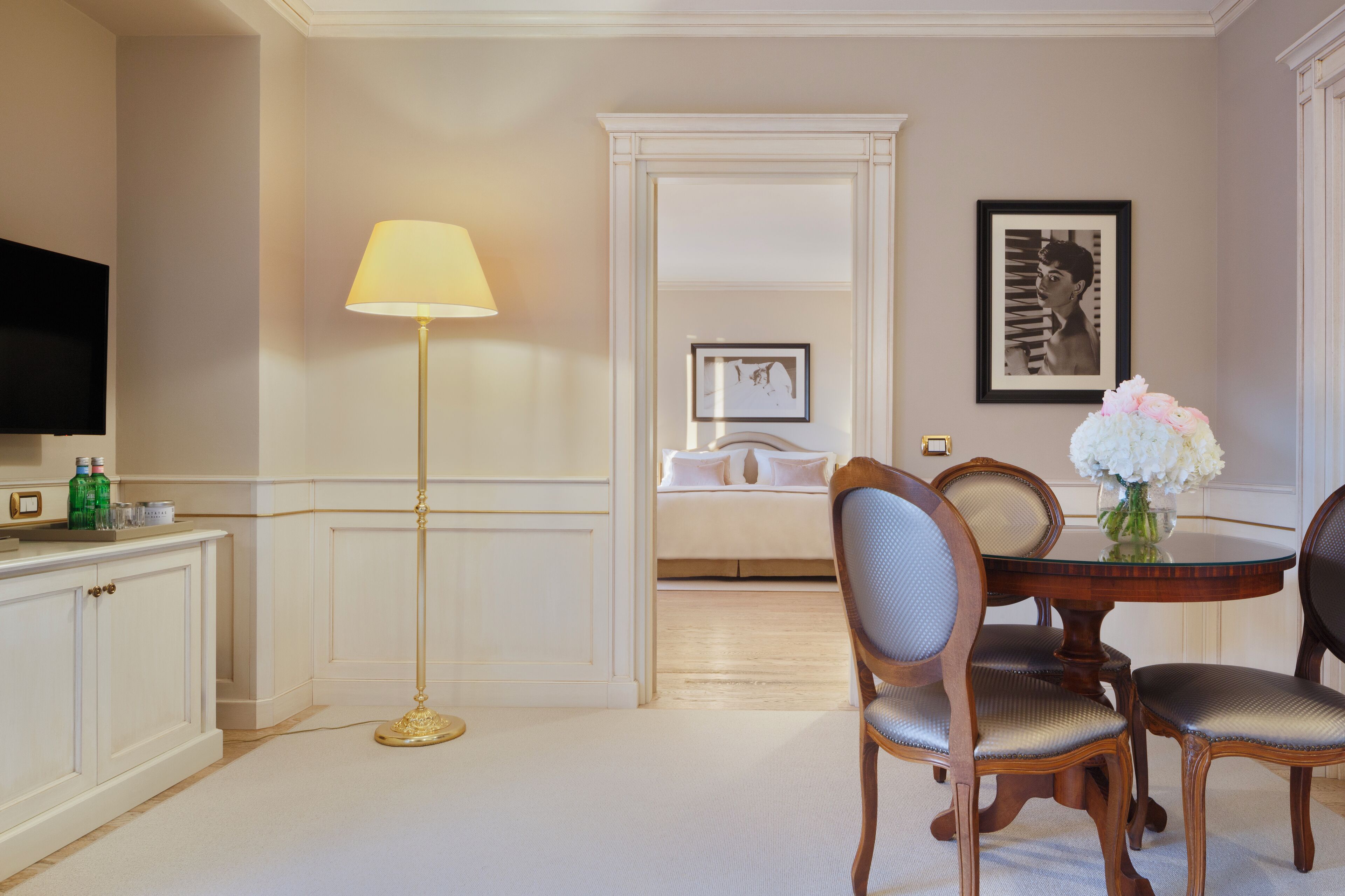 A dining area with a round table, two chairs, a floor lamp, and a television on a cabinet.