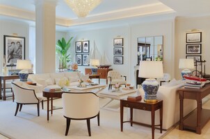 Un salón bien iluminado con un sofá blanco, sillones, una mesa de centro y una estantería. Hay cuadros enmarcados en las paredes y un espejo grande.