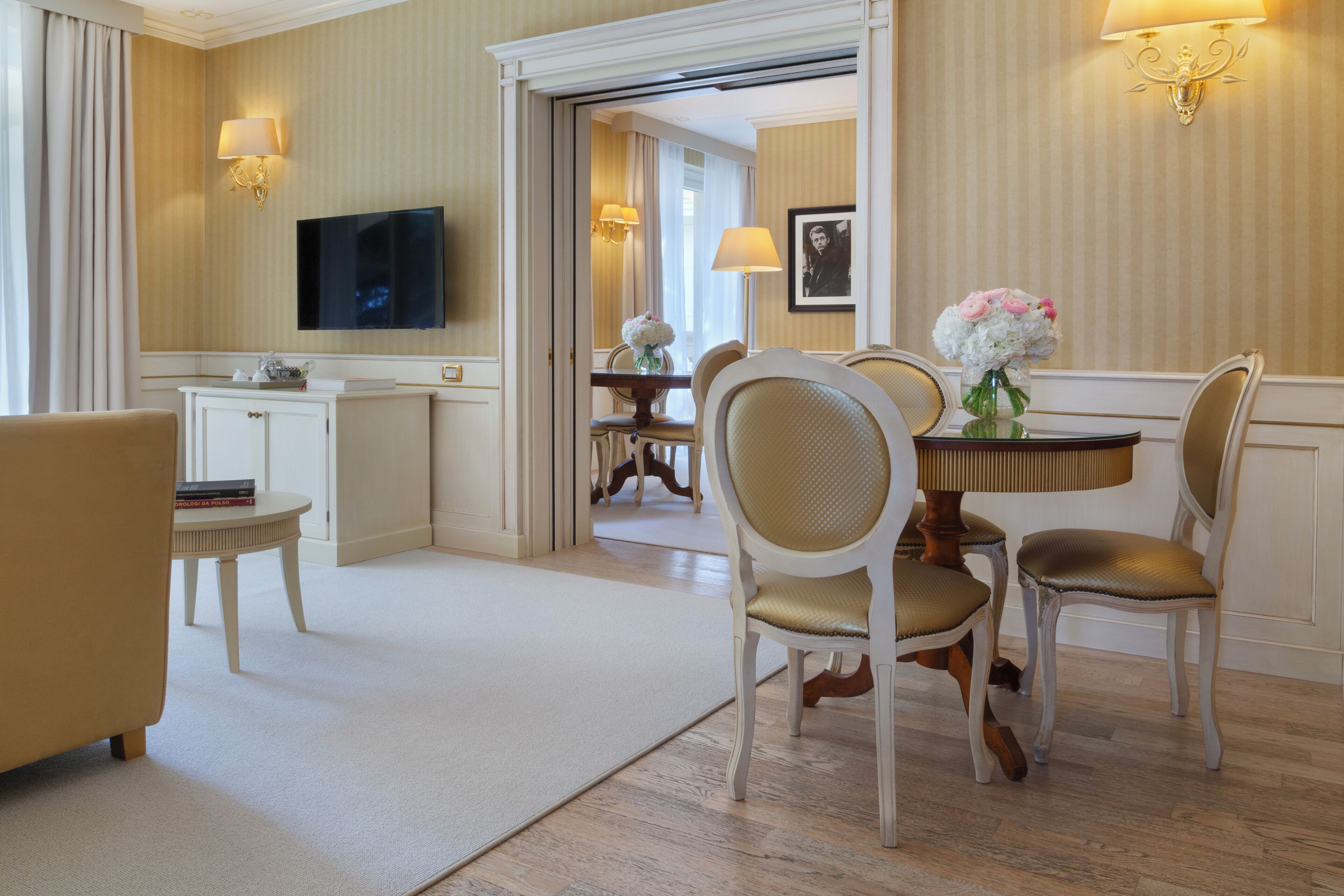 A hotel room with a dining area, a television, and a view of the hallway.