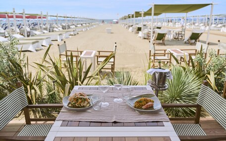 A beachside dining area with tables and chairs, a view of the beach, and a table set with plates of food and glasses.