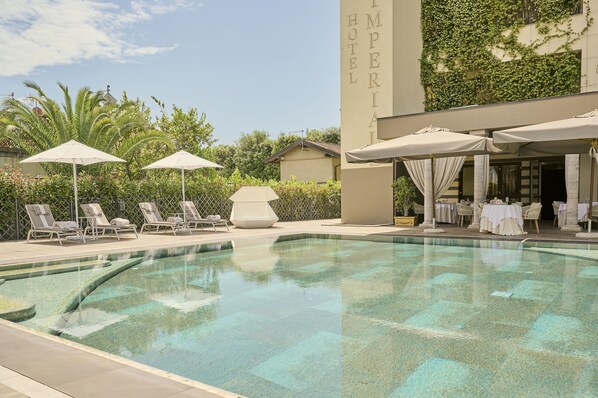 A pool area with lounge chairs and umbrellas, a building with "IMPERIAL HOTEL" signage, and a clear sky.