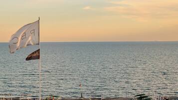 A pier with rows of beach chairs and umbrellas, a flag, and a view of the sea.