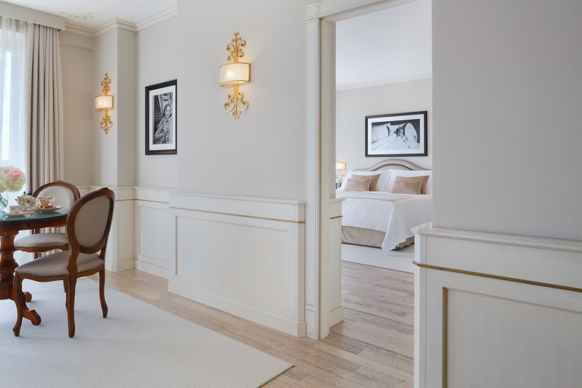 A hotel room with a bed, a dining area with a table and chairs, and wall-mounted lighting fixtures.