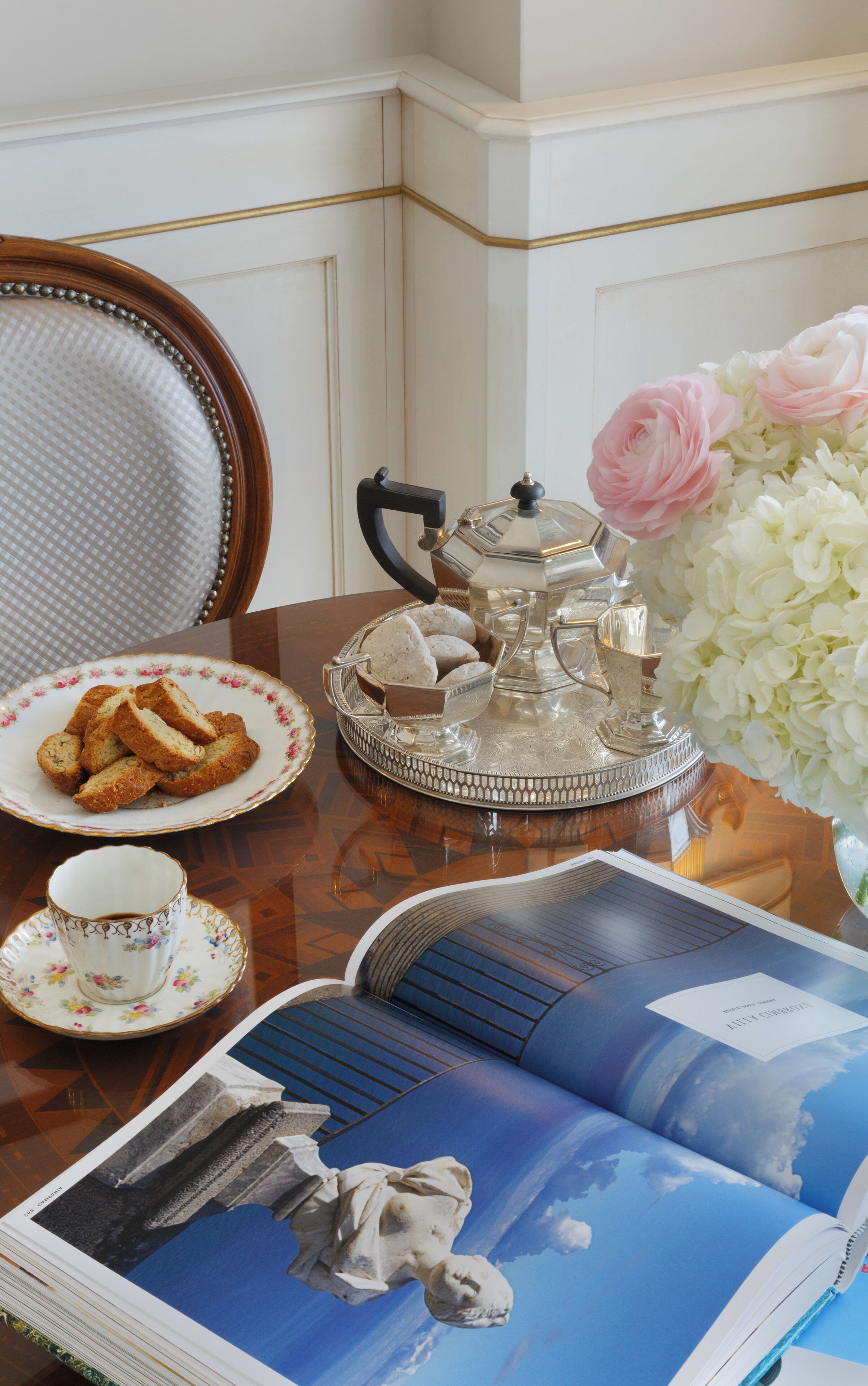 A table with a tea set, a plate of cookies, a cup, and a book.