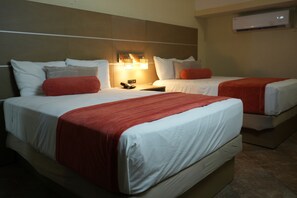 Dos camas con sábanas blancas y detalles en rojo, una mesita de noche con teléfono y un equipo de aire acondicionado en la pared.
