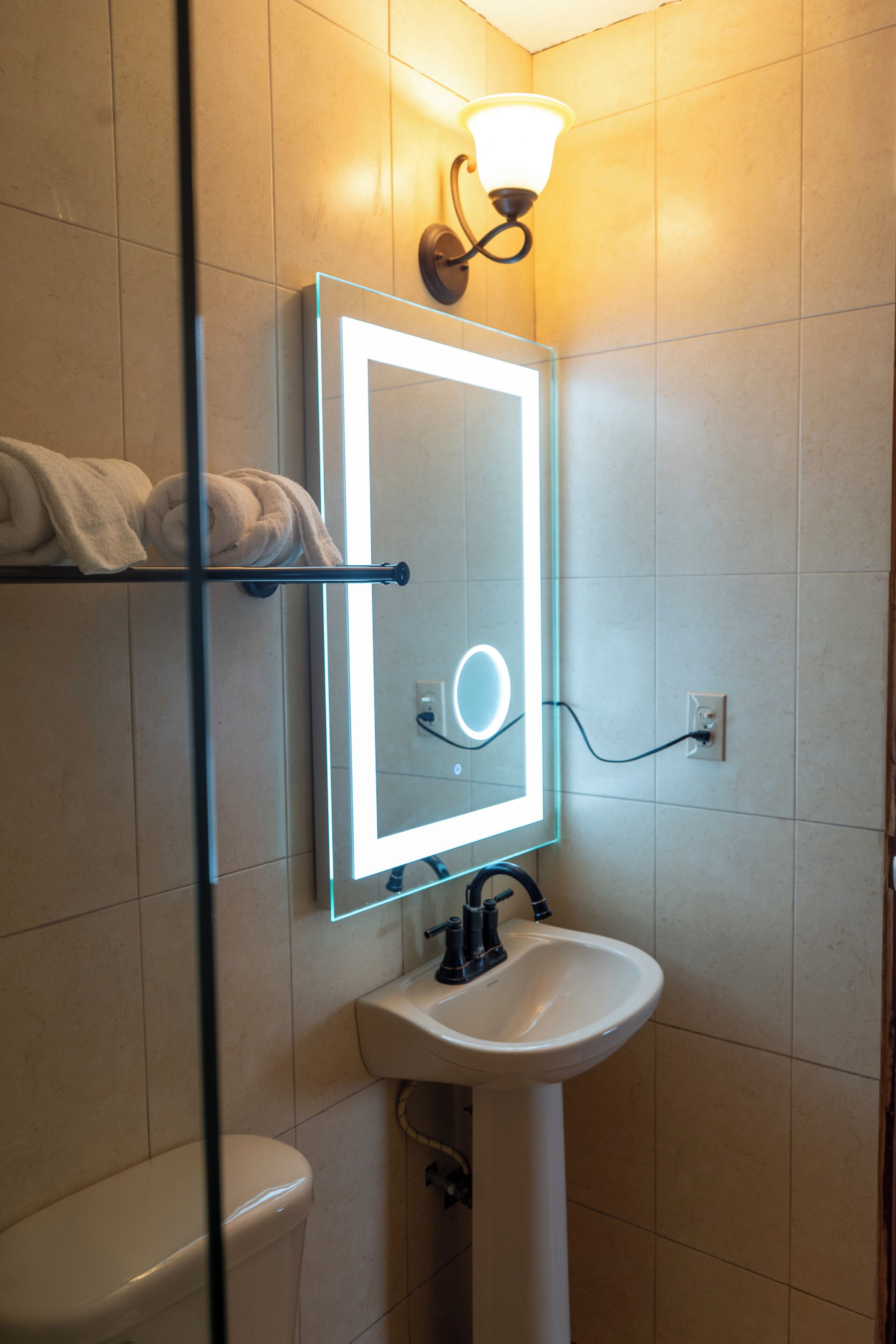 A bathroom with a white sink, a mirror with a light, and a towel rack.