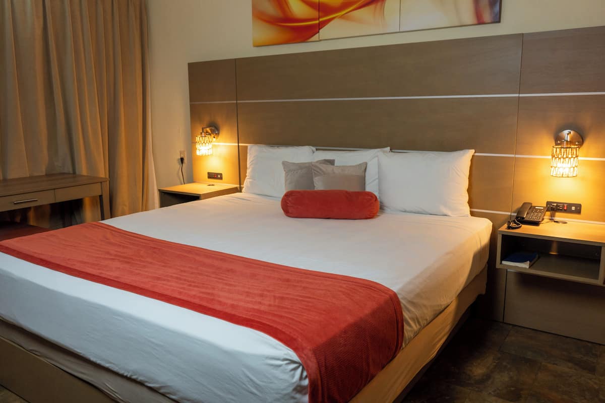 A hotel room with a large bed, two bedside tables, a nightstand, and a wall-mounted light fixture.