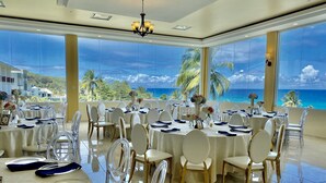 A banquet hall with round tables, white chairs, and a view of the ocean. - Hotel El Guajataca (Quebradillas)