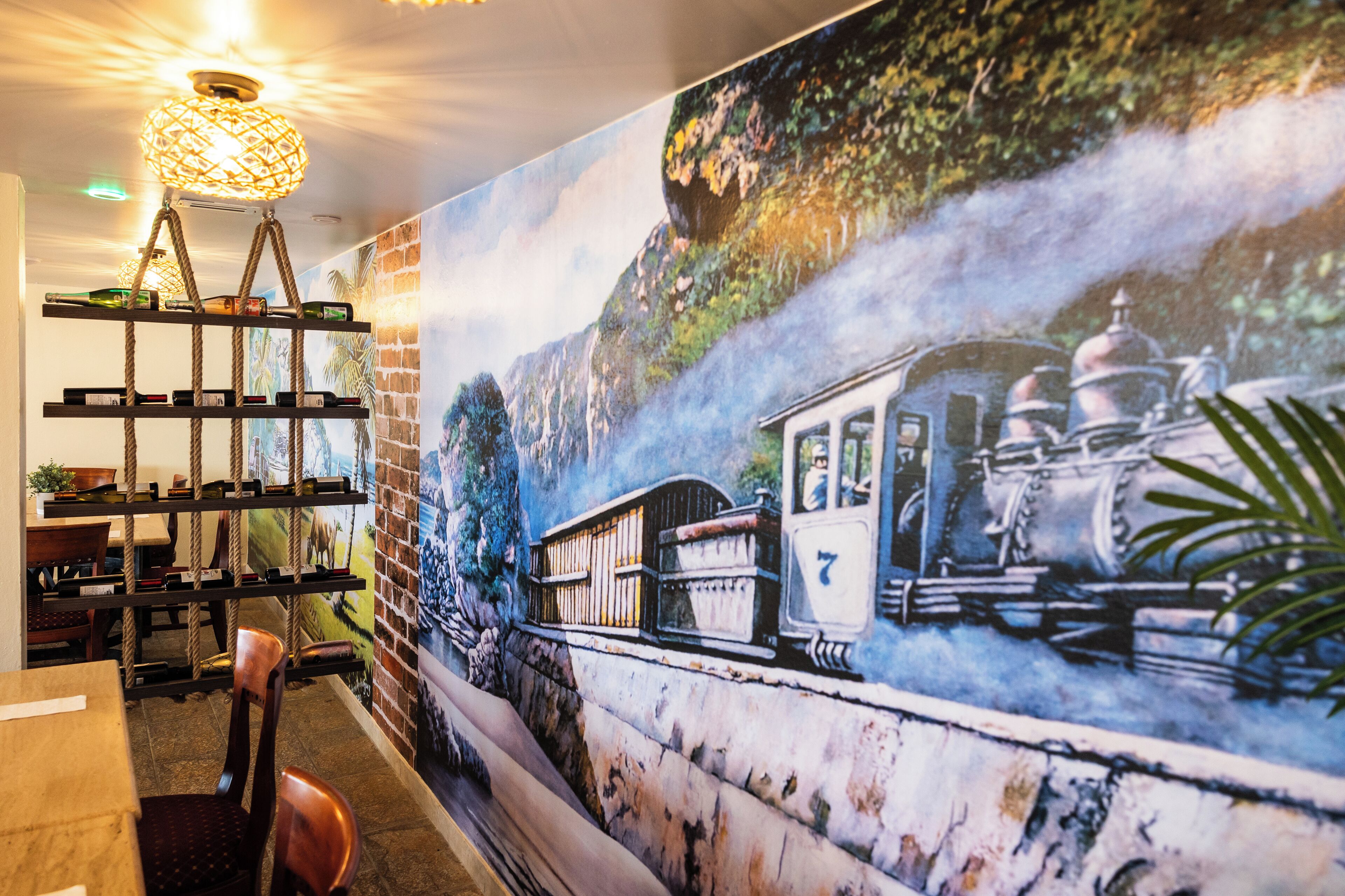 A mural of a train on a bridge, shelves with bottles, and a hanging light fixture.