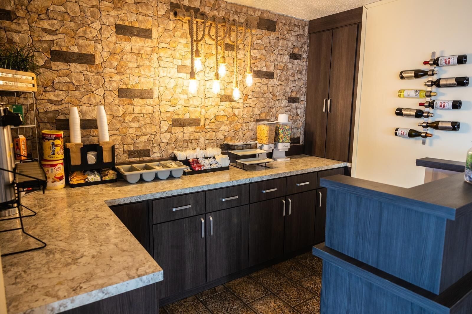 Una cocina con pared de piedra, armarios de madera, encimera de mármol y una estantería para vinos con varias botellas.