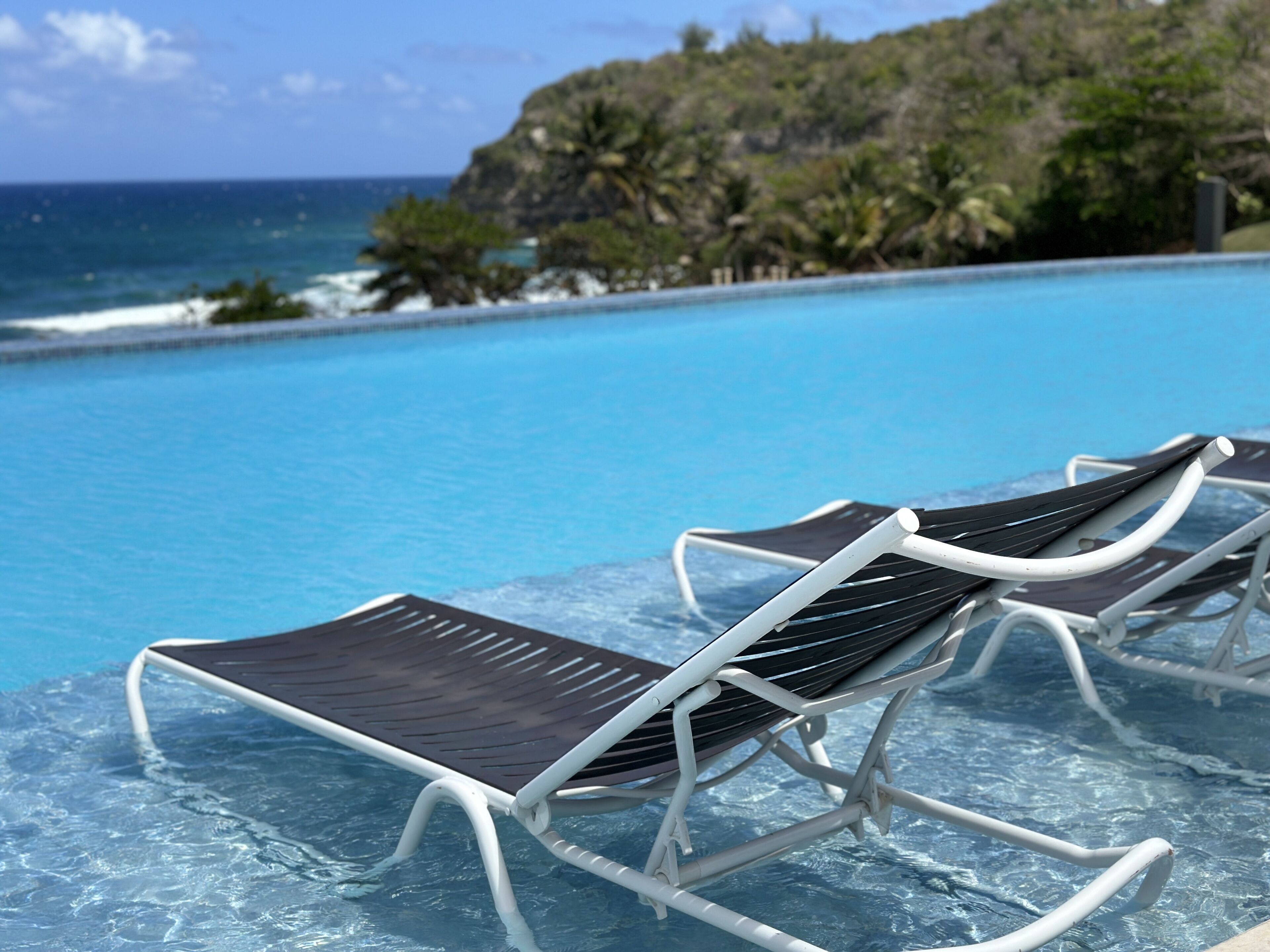 A poolside area with lounge chairs and a view of the ocean.