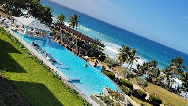 A pool area with a view of the ocean, surrounded by palm trees and a covered seating area. - Hotel El Guajataca (Quebradillas)