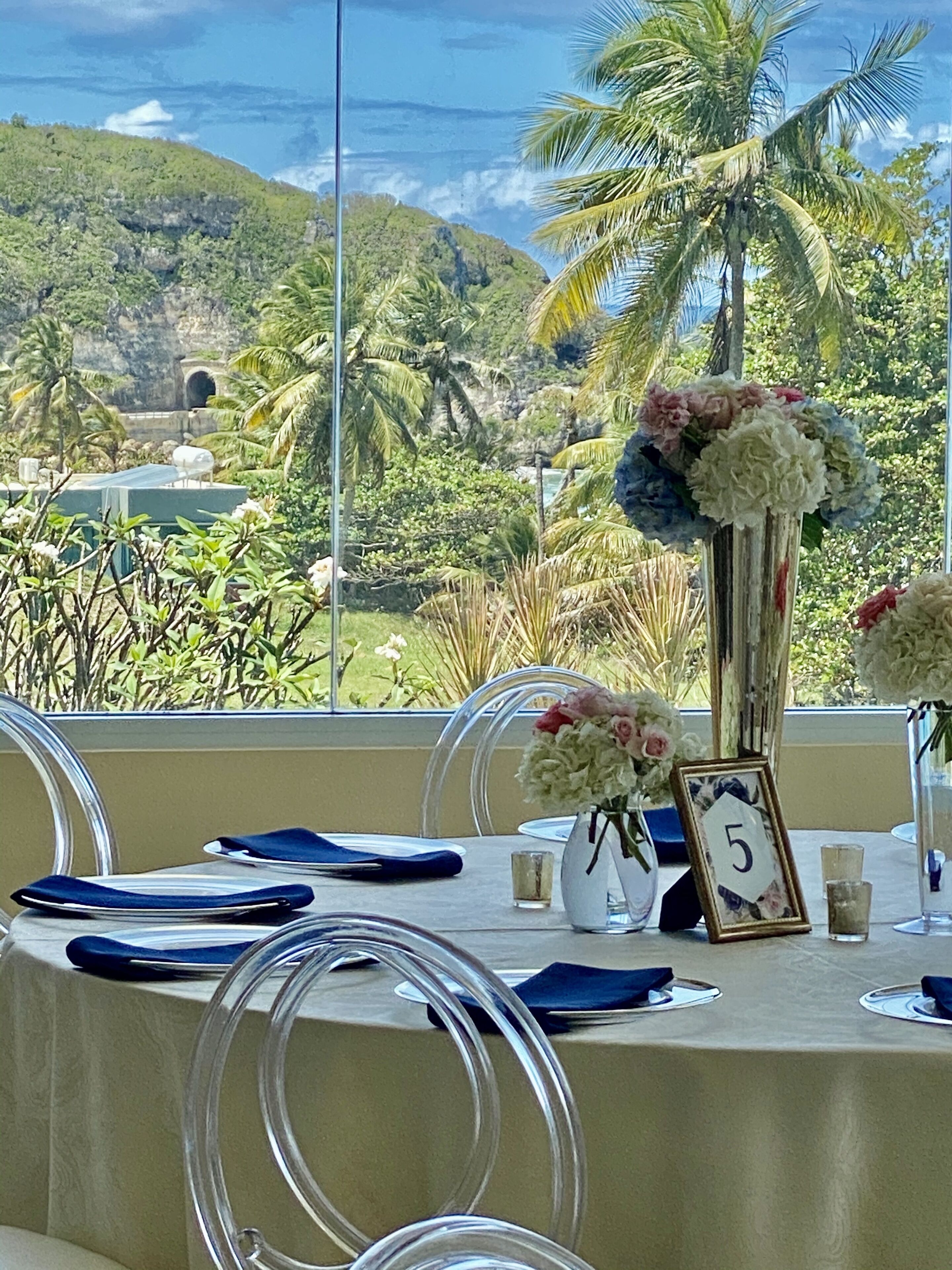 A table set with clear chairs, a floral centerpiece, and a number sign.