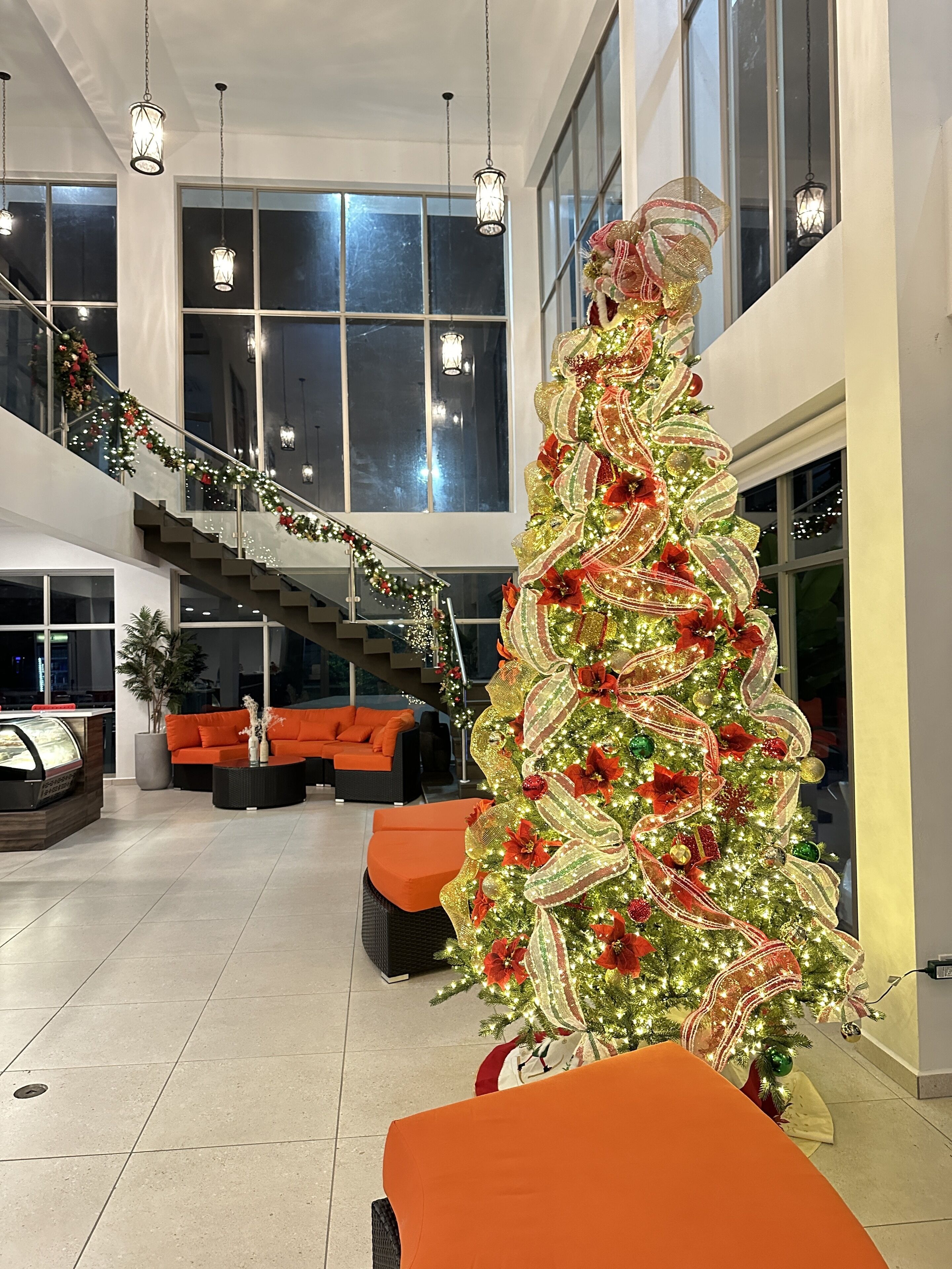 A spacious lobby with a large Christmas tree decorated with lights and ornaments, a staircase with festive garlands, and modern seating areas.