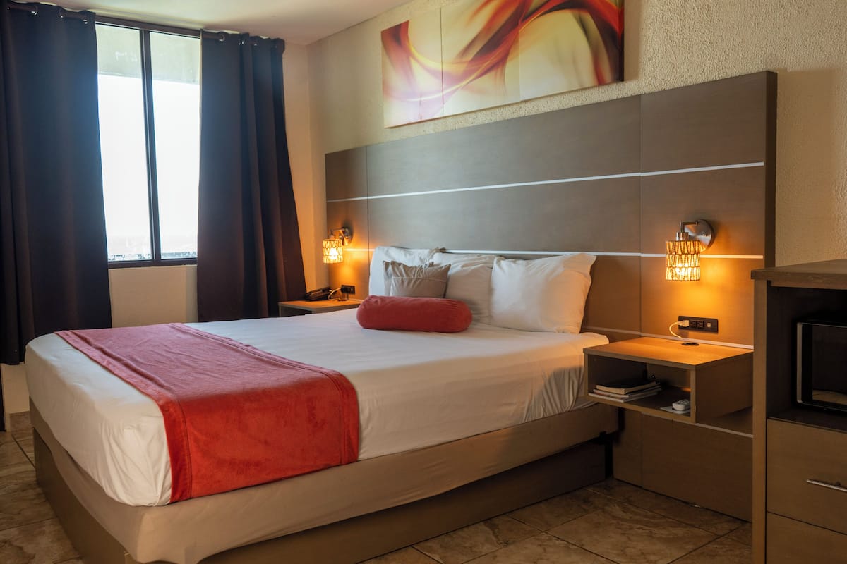 A hotel room with a bed, bedside lamps, a nightstand, a TV, and a window with curtains.