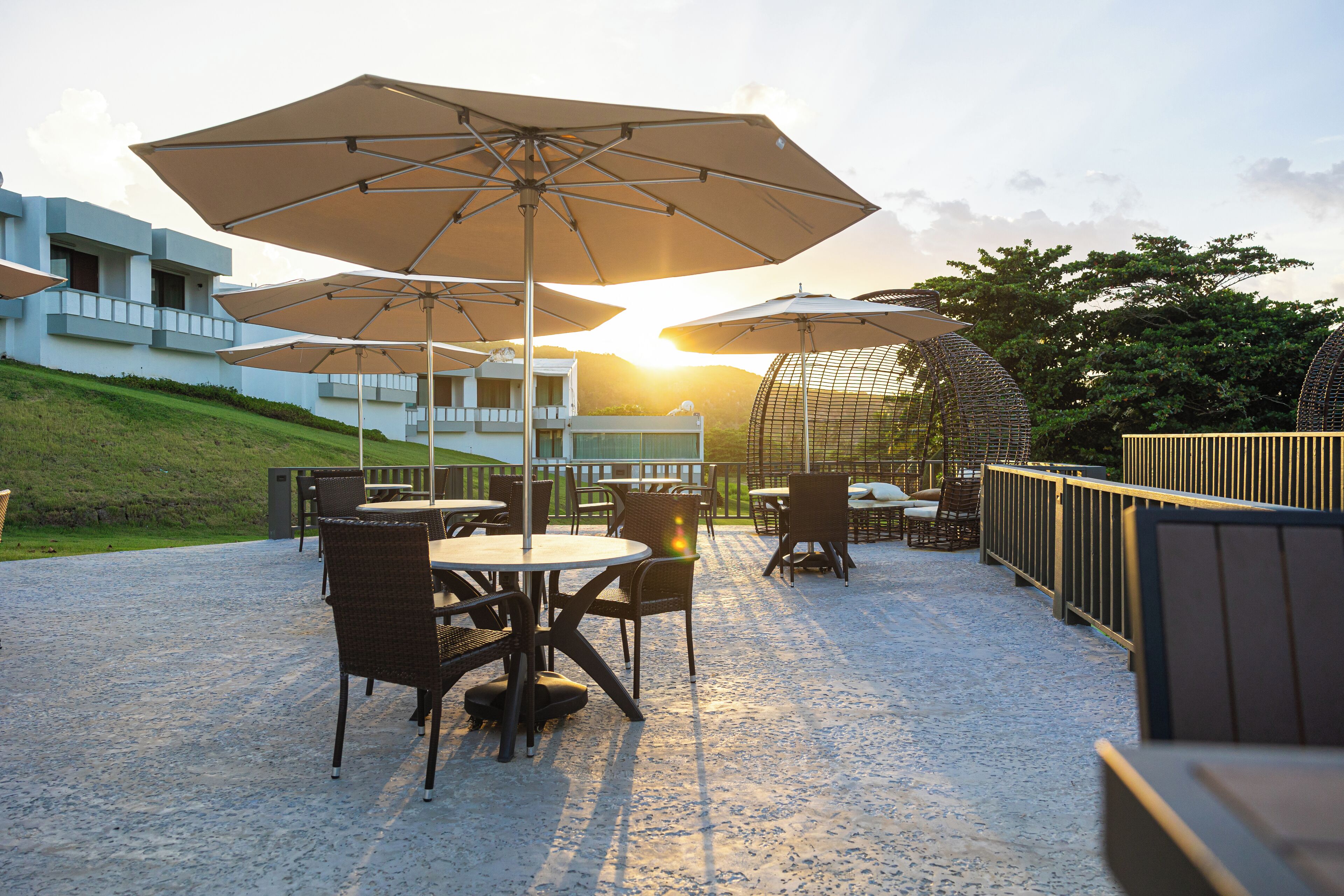 Un patio al aire libre con mesas, sillas, sombrillas y vistas al atardecer.