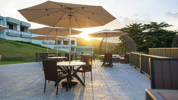 Un patio al aire libre con mesas, sillas, sombrillas y vistas al atardecer.