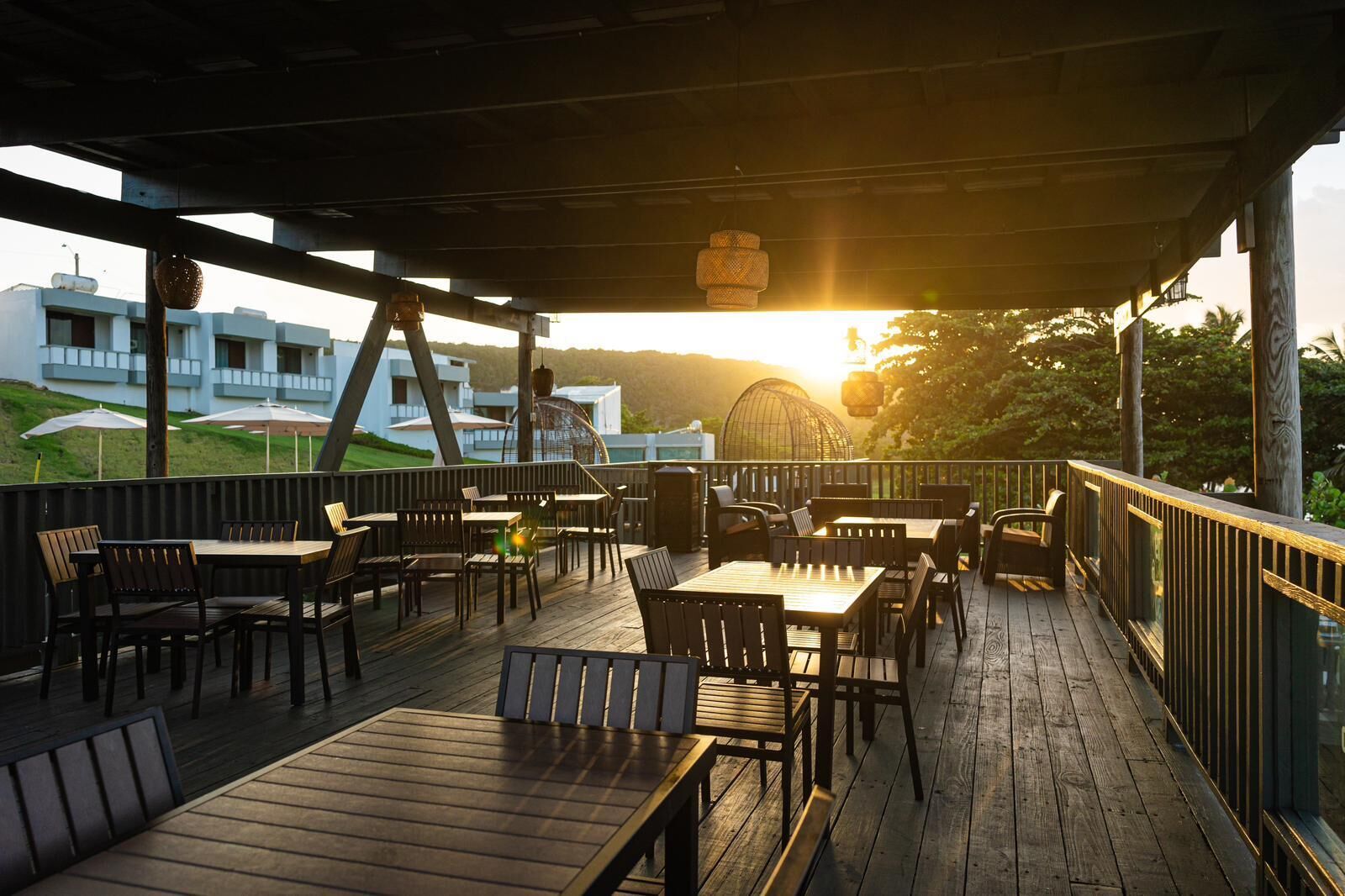 Une terrasse en bois, agrémentée de tables et de chaises, qui offre une vue sur un quartier résidentiel avec ses maisons et une colline.