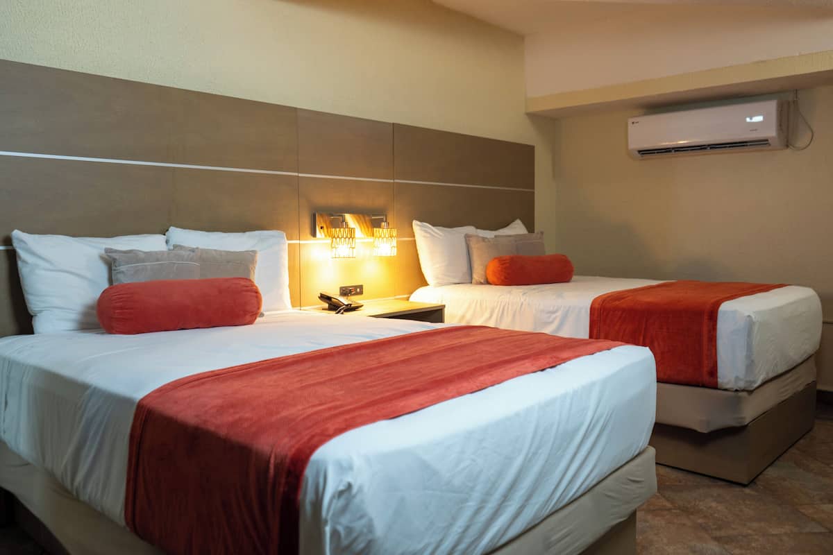 A hotel room with two beds, a nightstand, a lamp, and an air conditioning unit.