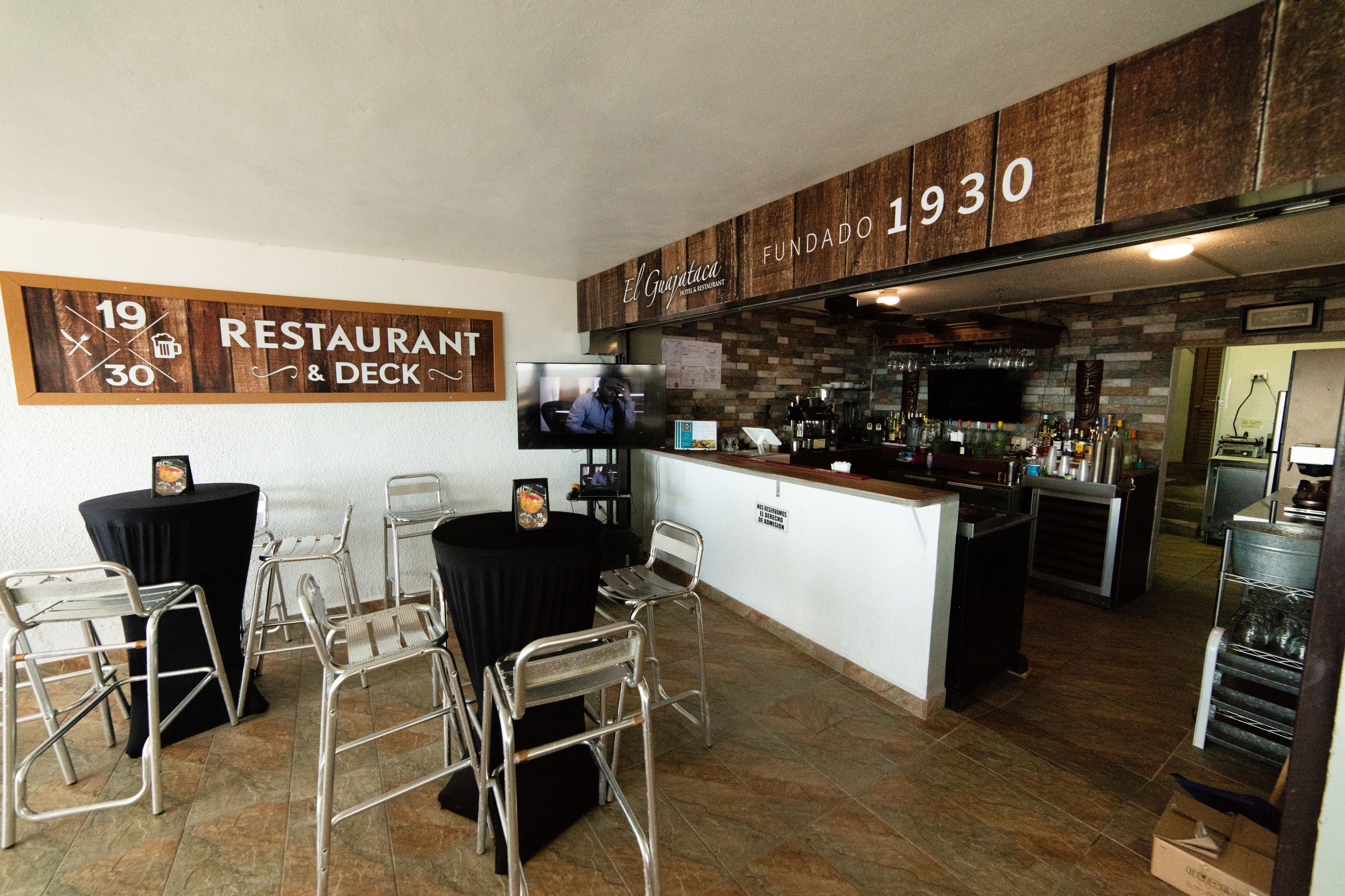A restaurant with a bar area, metal chairs, a television, and a wooden wall with the number 1930.