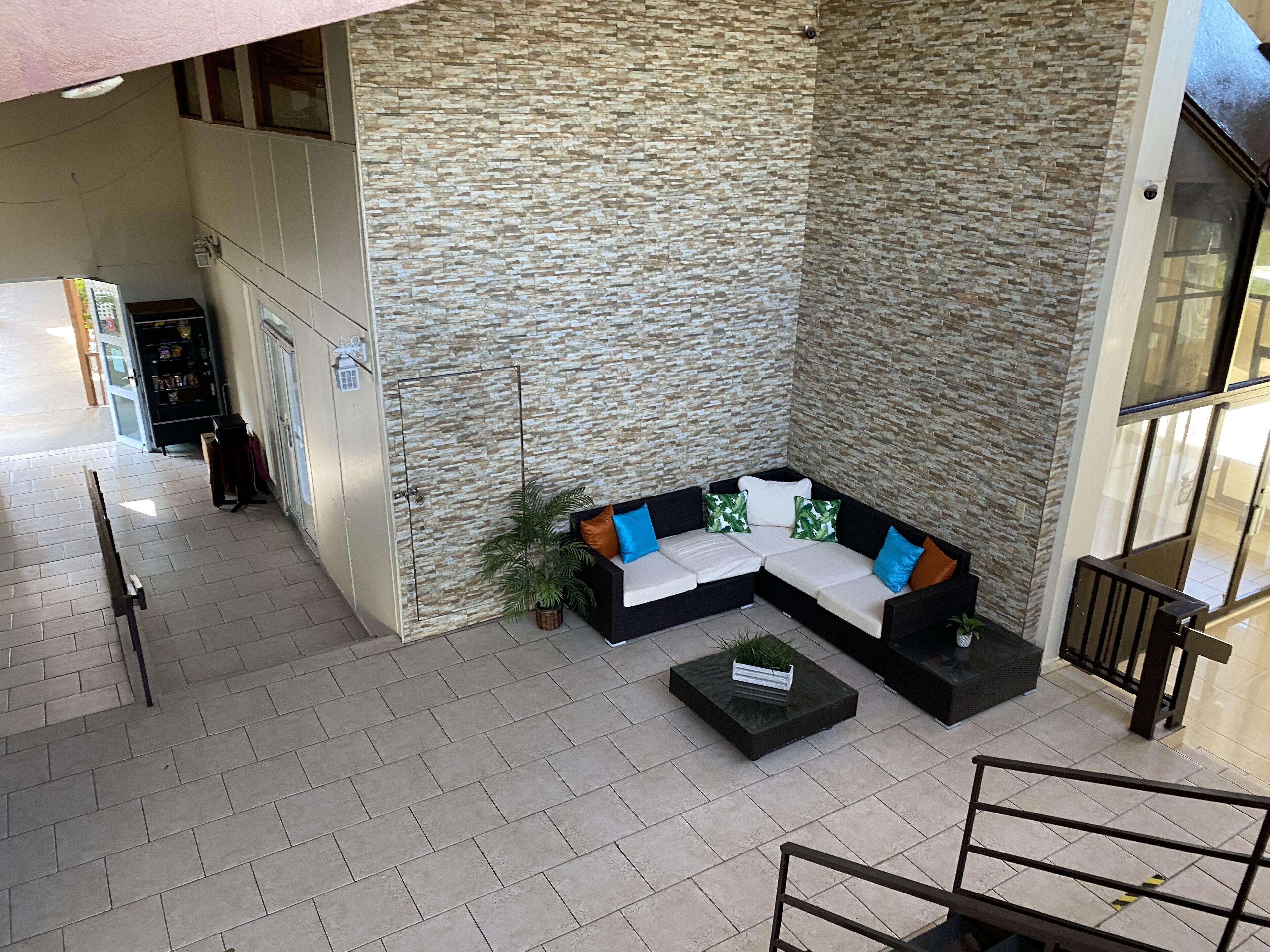 A modern indoor seating area with a stone-textured wall, a black sectional sofa with blue and white cushions, and a small black coffee table.
