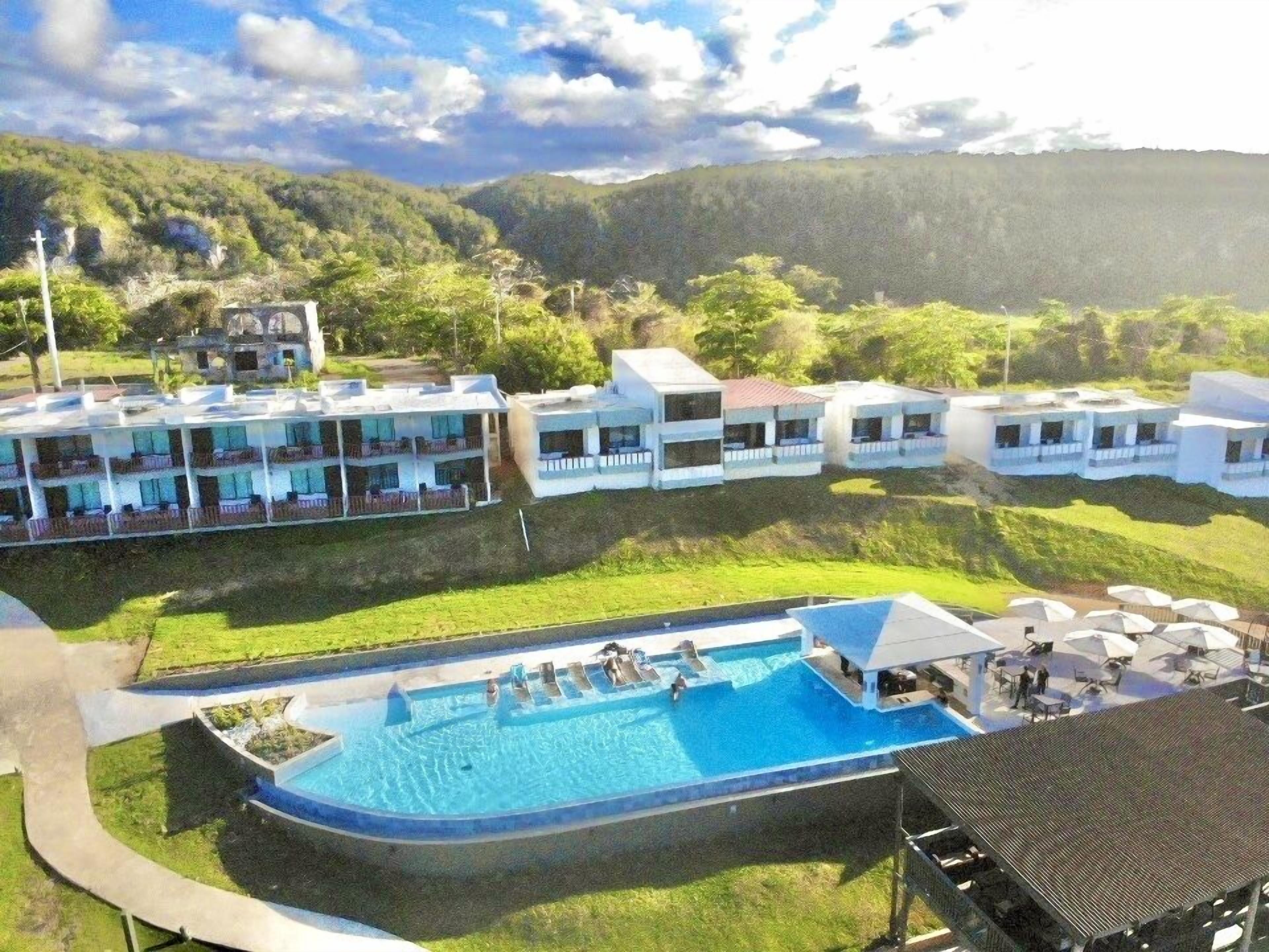 A resort with a swimming pool, multiple guest buildings, and a mountainous backdrop.