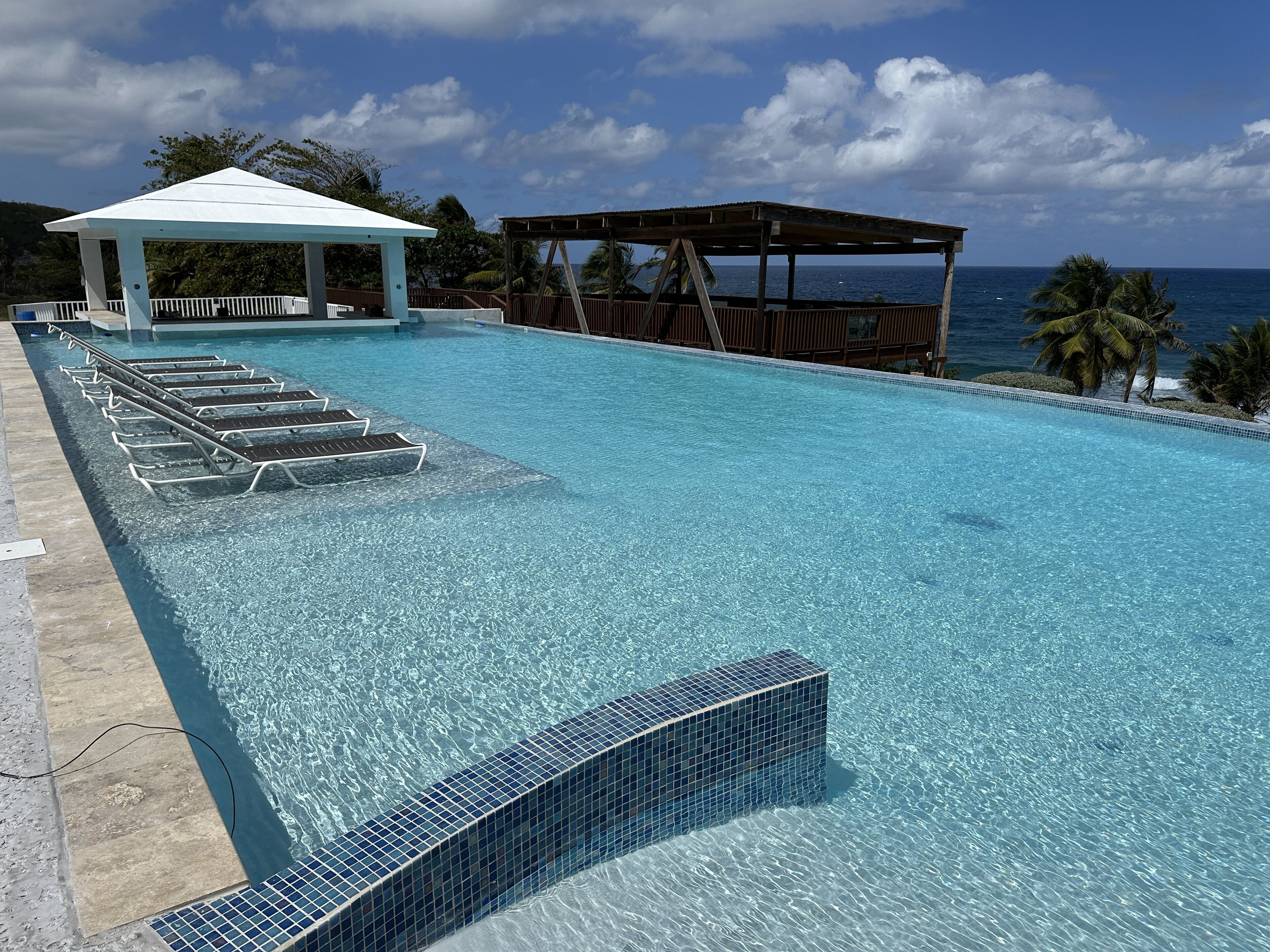 A clear blue pool with lounge chairs and a gazebo, overlooking the ocean.