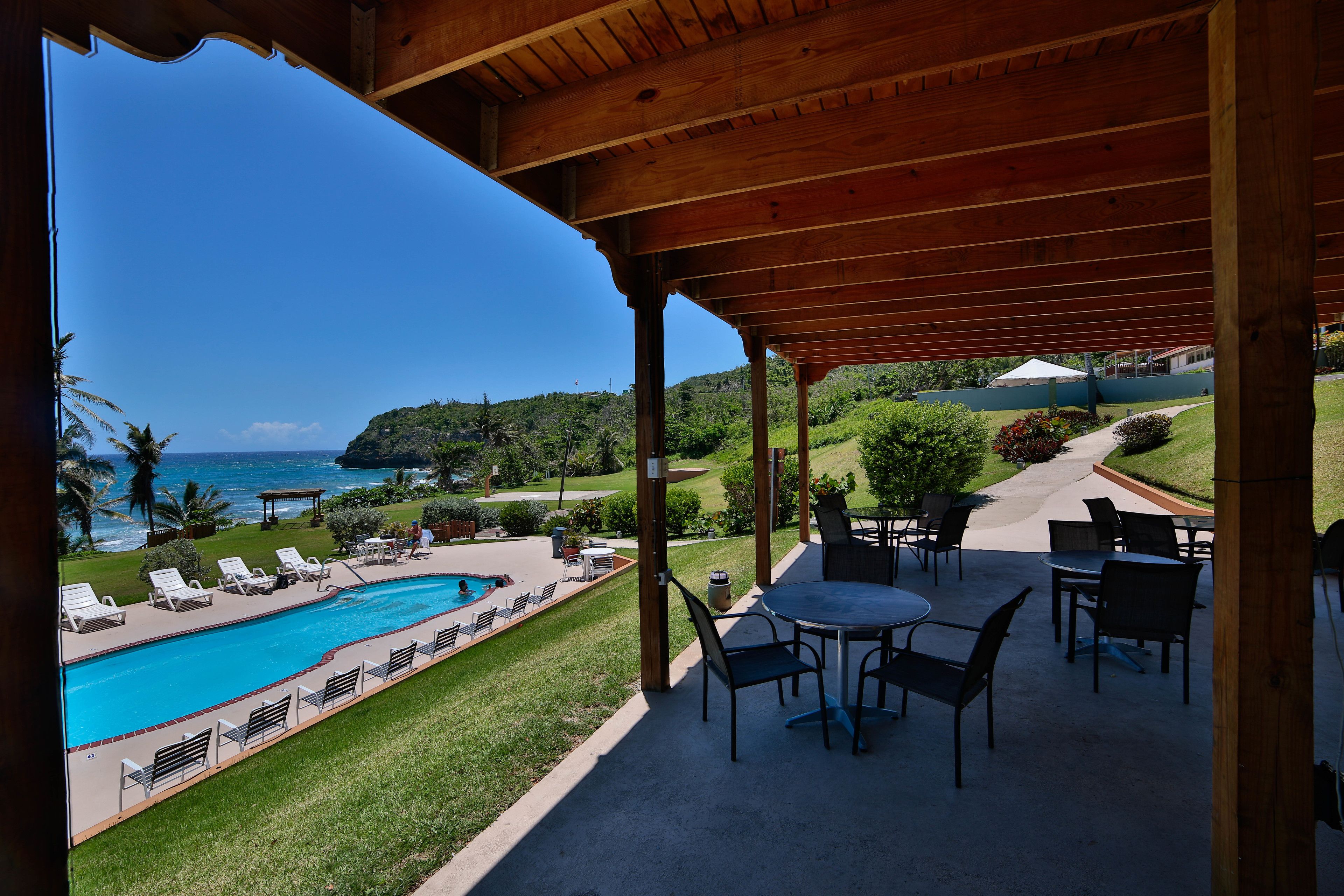 A covered outdoor area with a pool, lounge chairs, and tables.