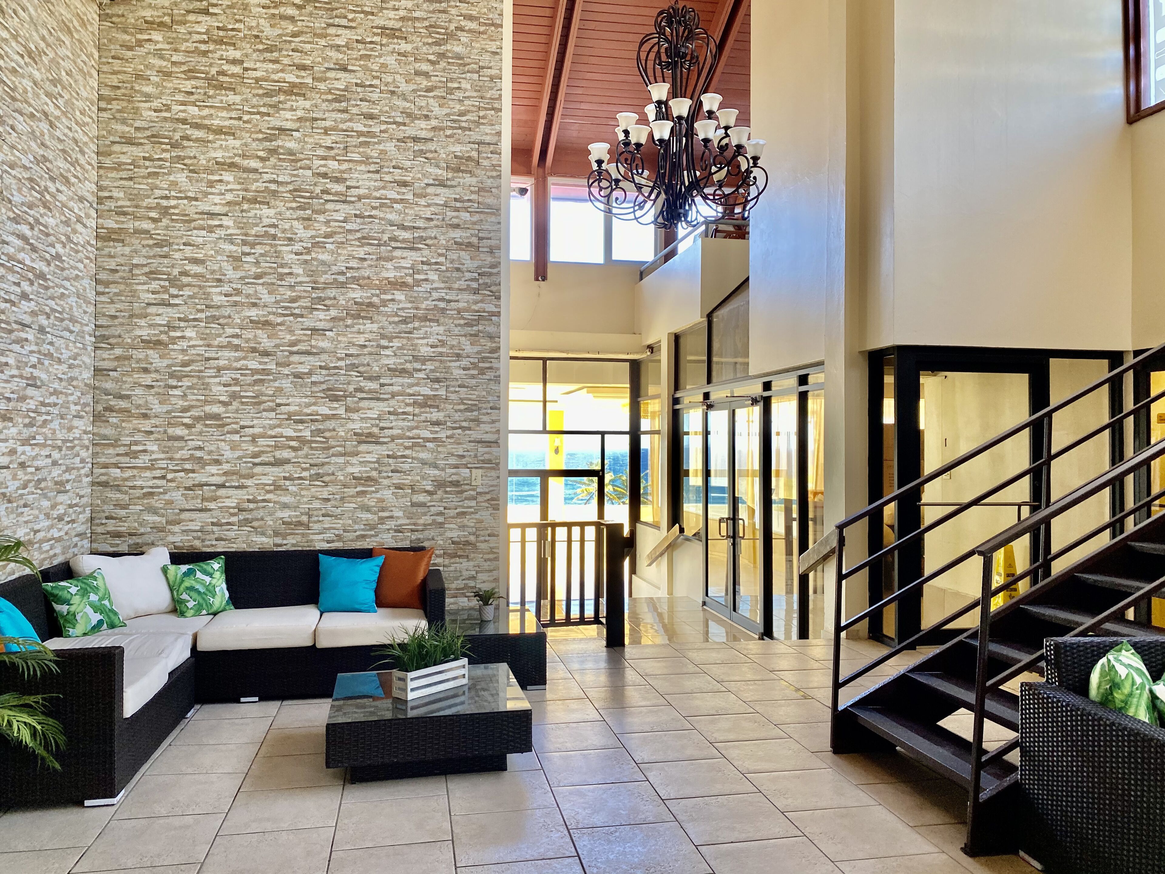 A spacious lobby with a stone accent wall, a sectional sofa with colorful cushions, a glass coffee table, and a staircase with a metal railing.