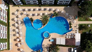 An aerial view of a resort with a large swimming pool, sun loungers, and a parking area.