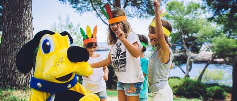 A mascot in a park with trees and a body of water in the background.